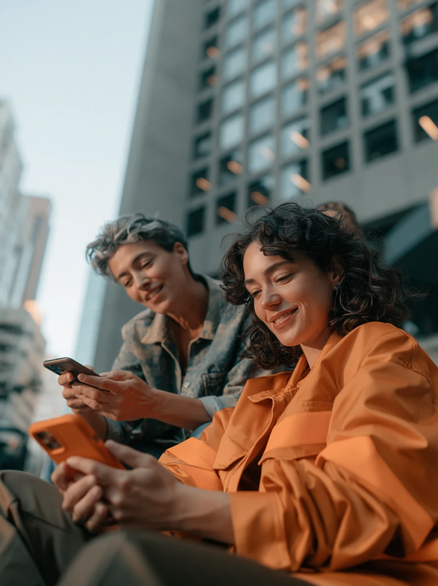 Duas amigas sorrindo enquanto usam o celular