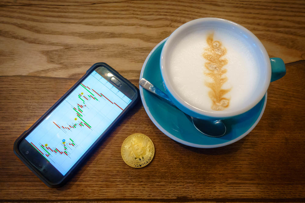 Copo de café moeda de bitcoin e celular com gráficos